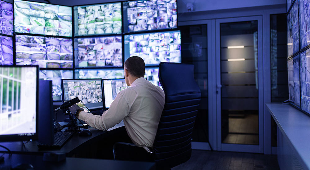 Mature adult man working in surveillance, security and guarding agency and looking at many monitors in front of him.